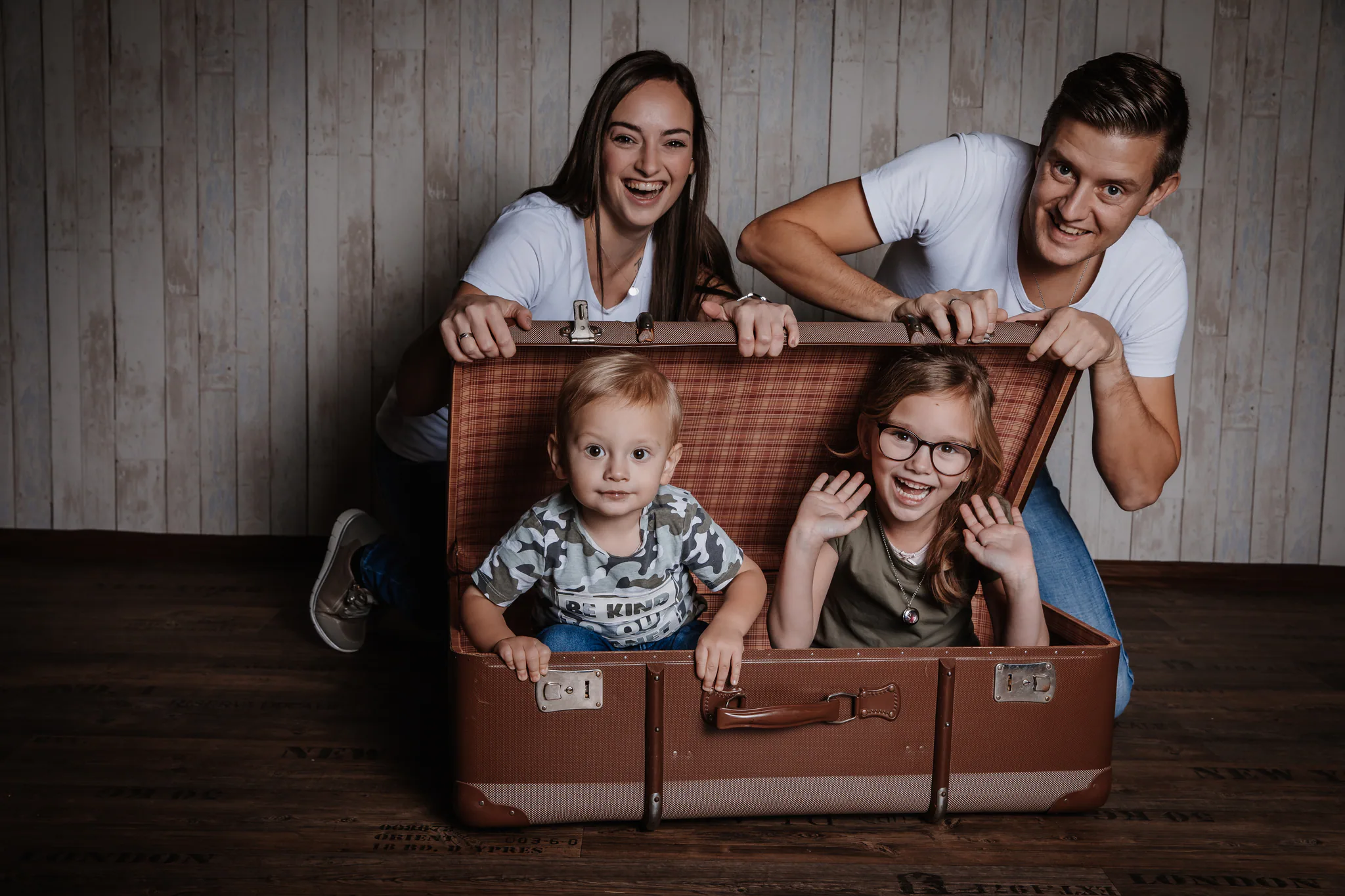 Familie posiert spielerisch mit einem großen Koffer im Studio